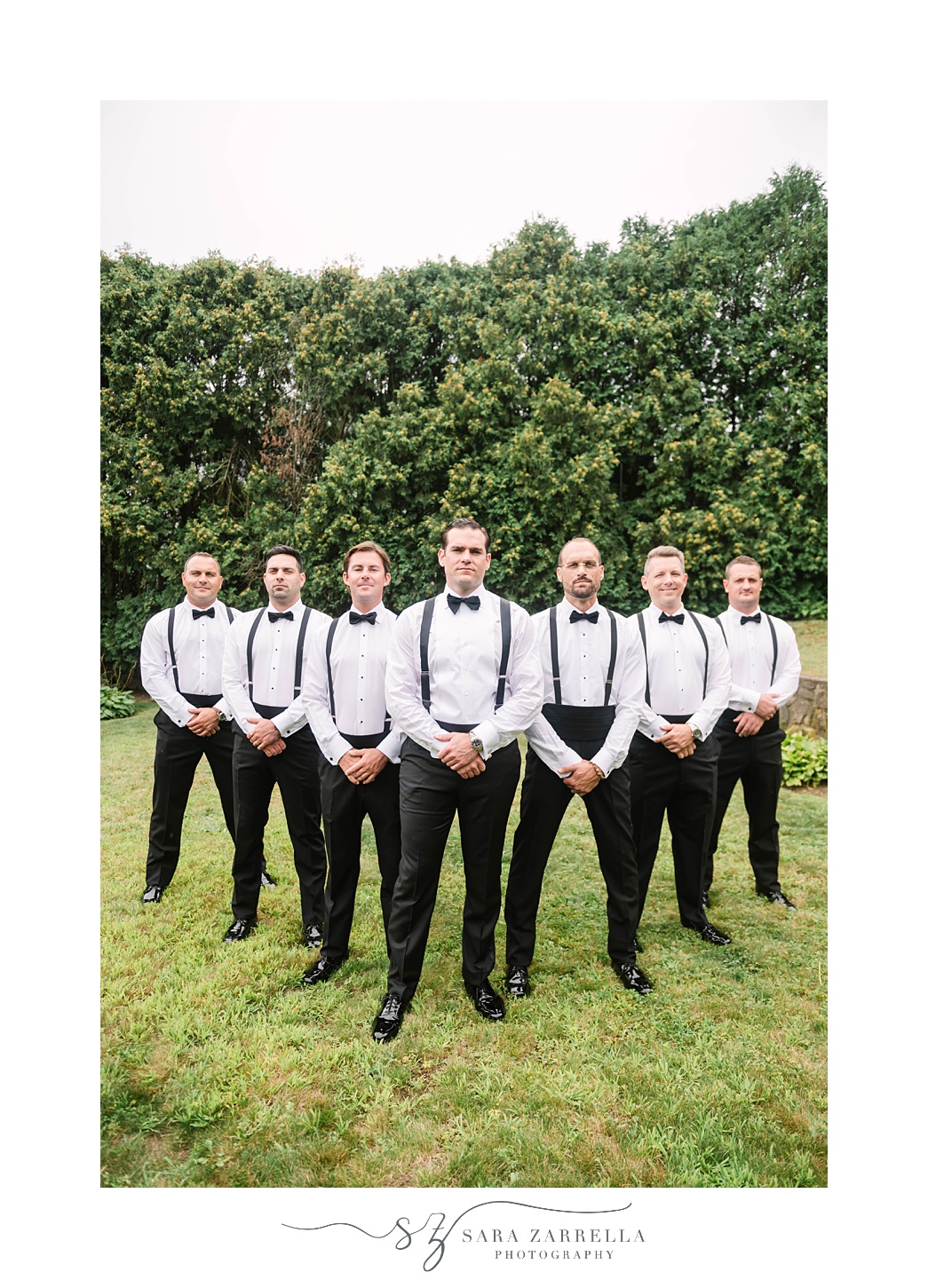 groom poses with groomsmen in suspenders 