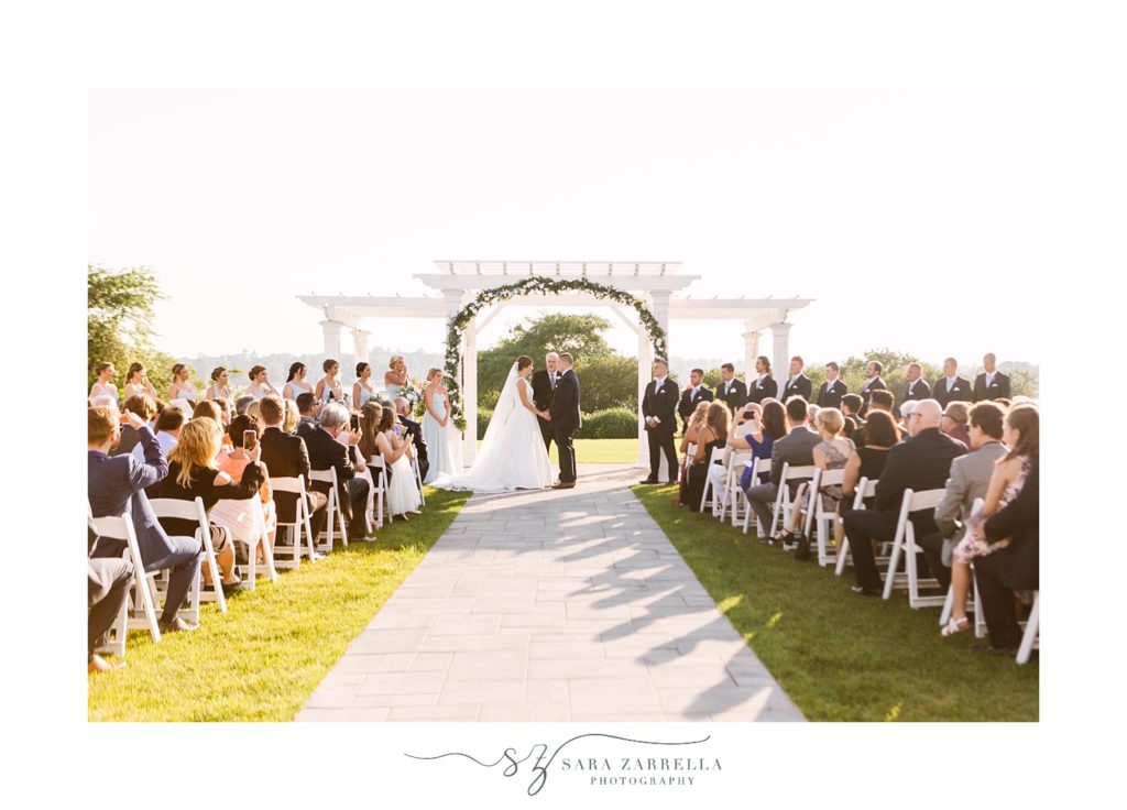 bride and groom hold hands under white arbor in Newport RI