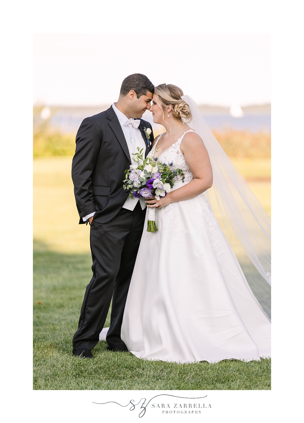 newlyweds stand touching noses by waterfront at Quidnessett Country Club