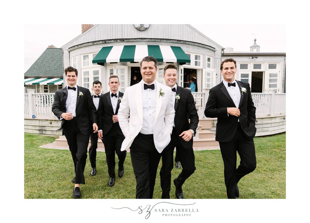 groom walks with groomsmen in front of The Dunes Club