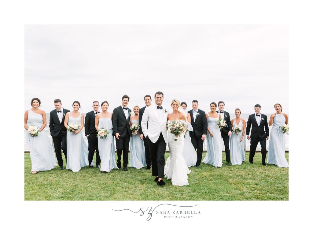 bride and groom walk with wedding party in black and blue along Narragansett Bay