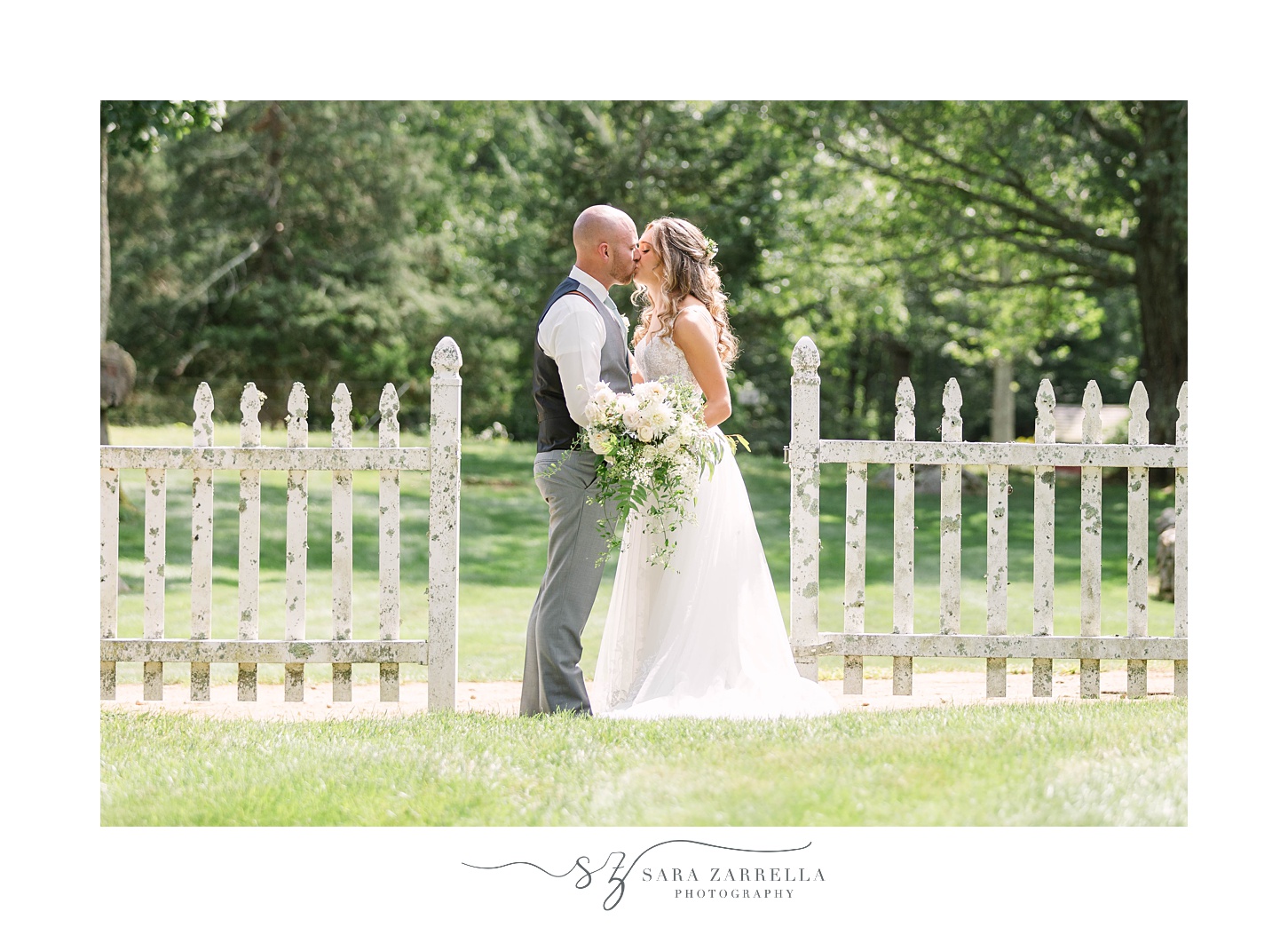 bride and groom kiss between white fence on Rhode Island farm