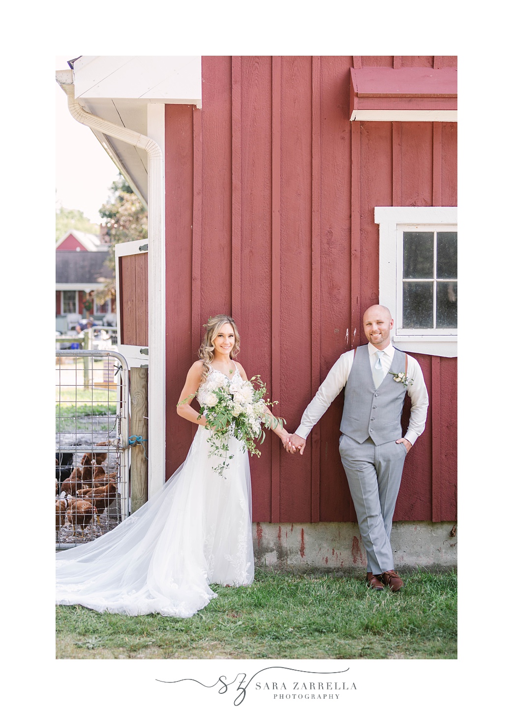 couple holds hands leaning against red barn