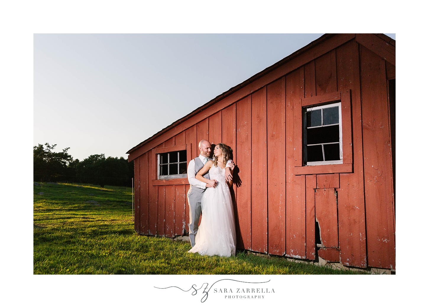 bride and groom pose by red barn during RI wedding photos