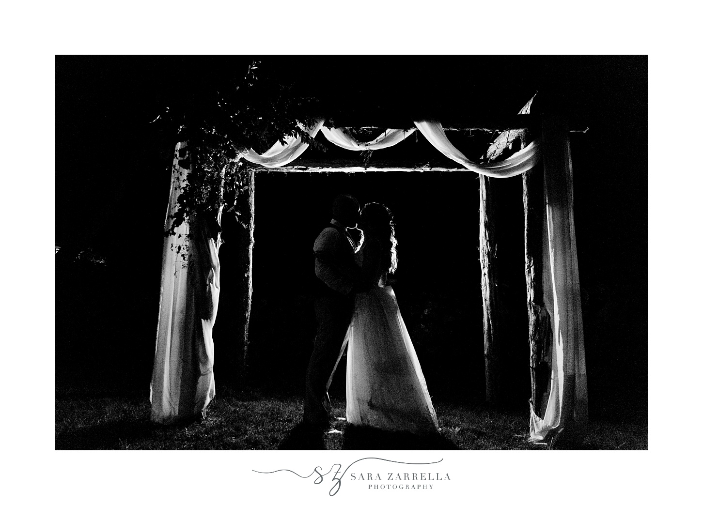 couple kisses under wooden arch on RI farm at night