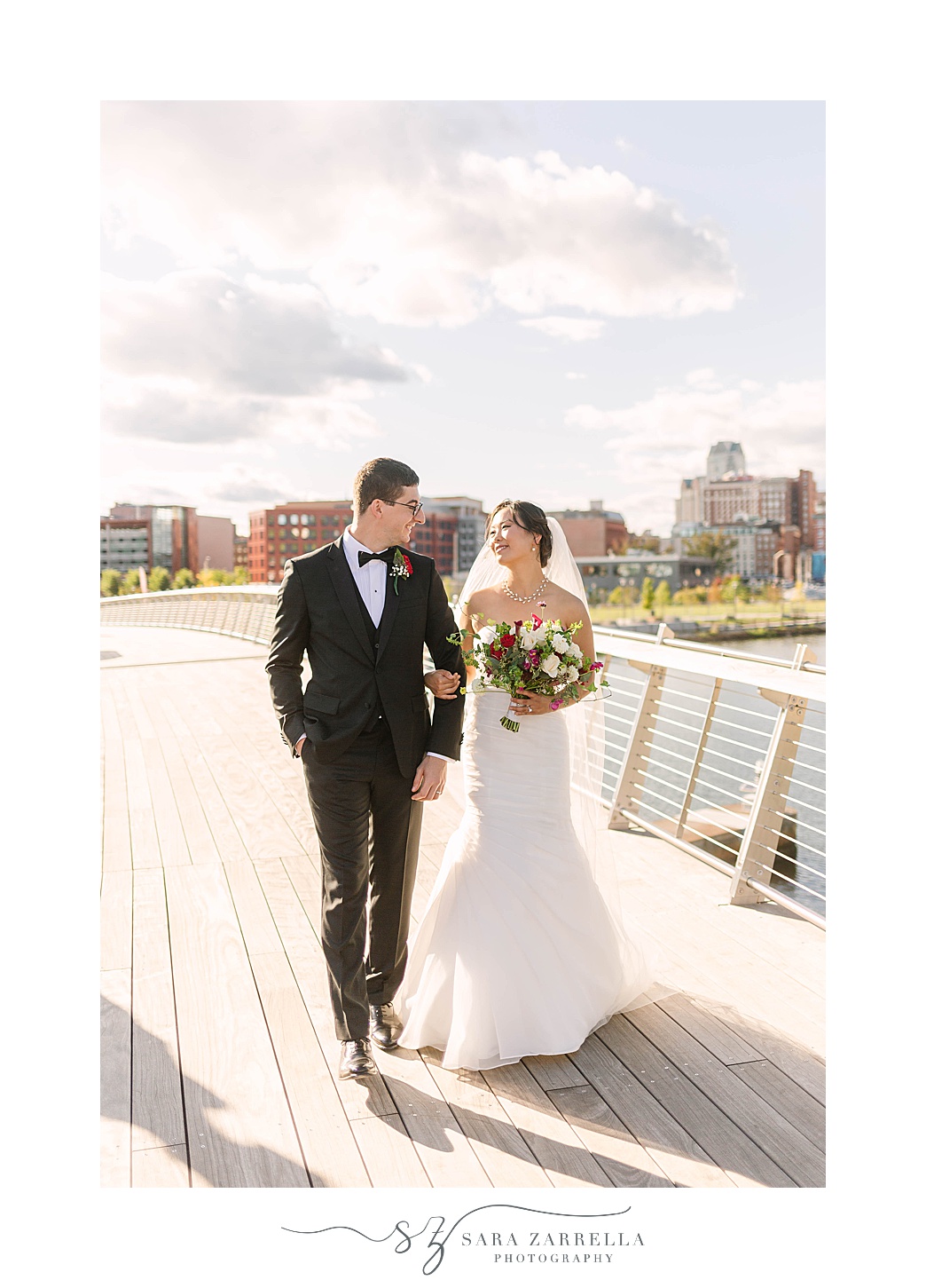 newlyweds hold hands walking on bridge during Downtown Providence wedding photos