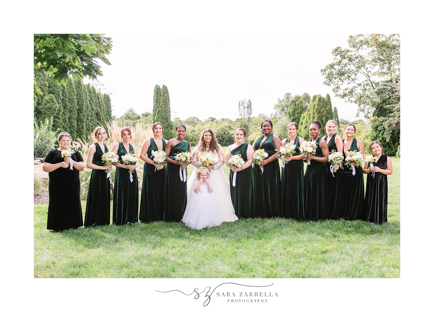 bride and bridesmaids in green gown pose in grassy field 