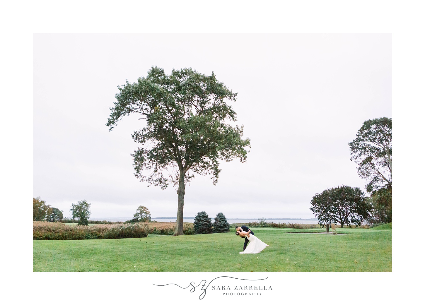 groom dips bride while kissing by tree at Quidnessett Country Club