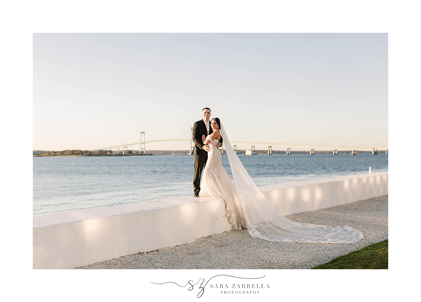bride and groom pose on wall during portraits at Belle Mer with bride's veil draped down