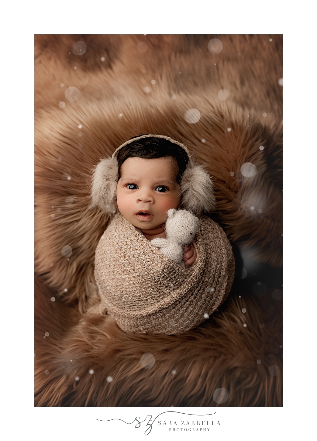 baby lays in brown wrap with earmuffs