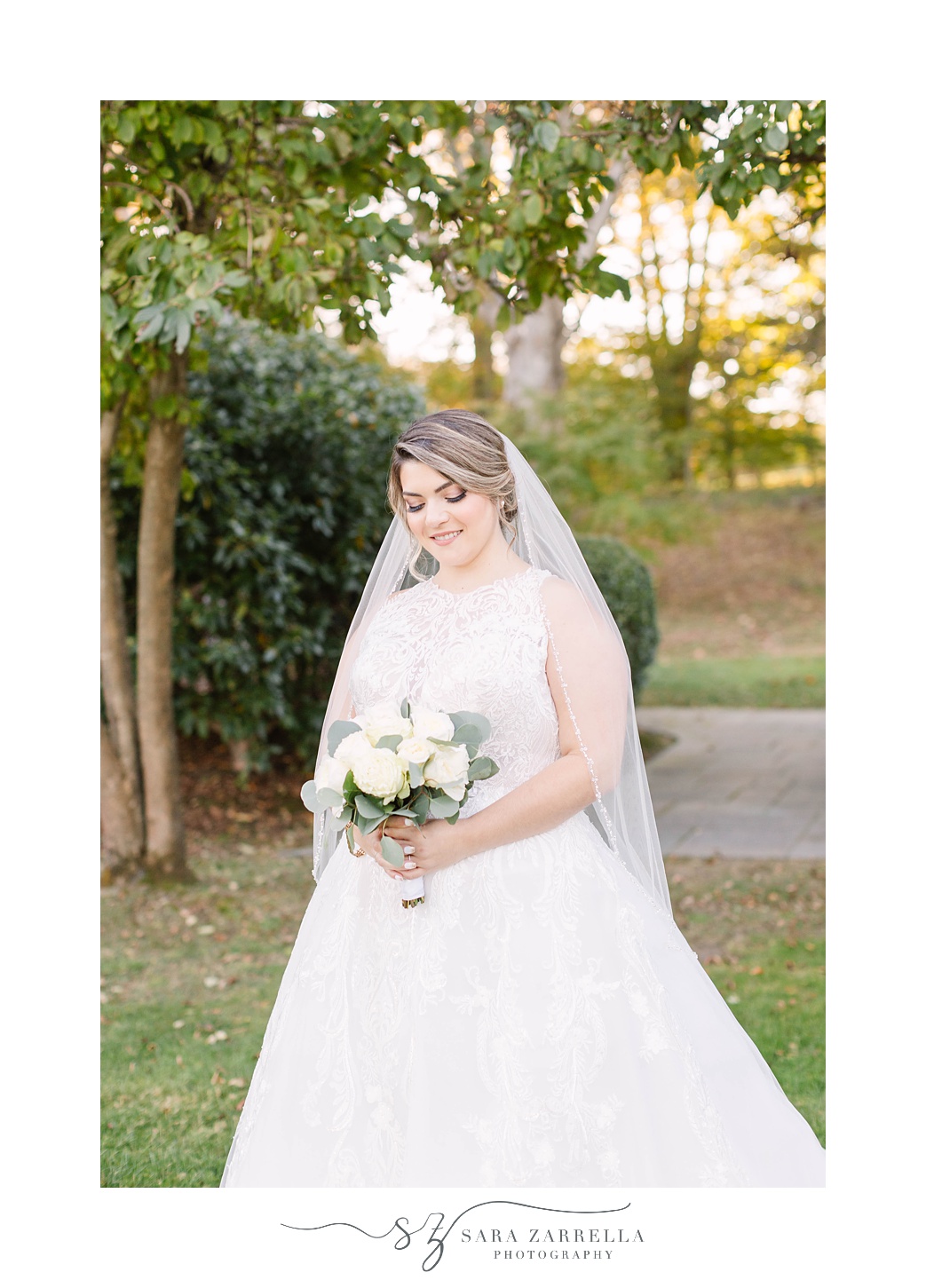 bride looks down at white bouquet with veil around shoulders