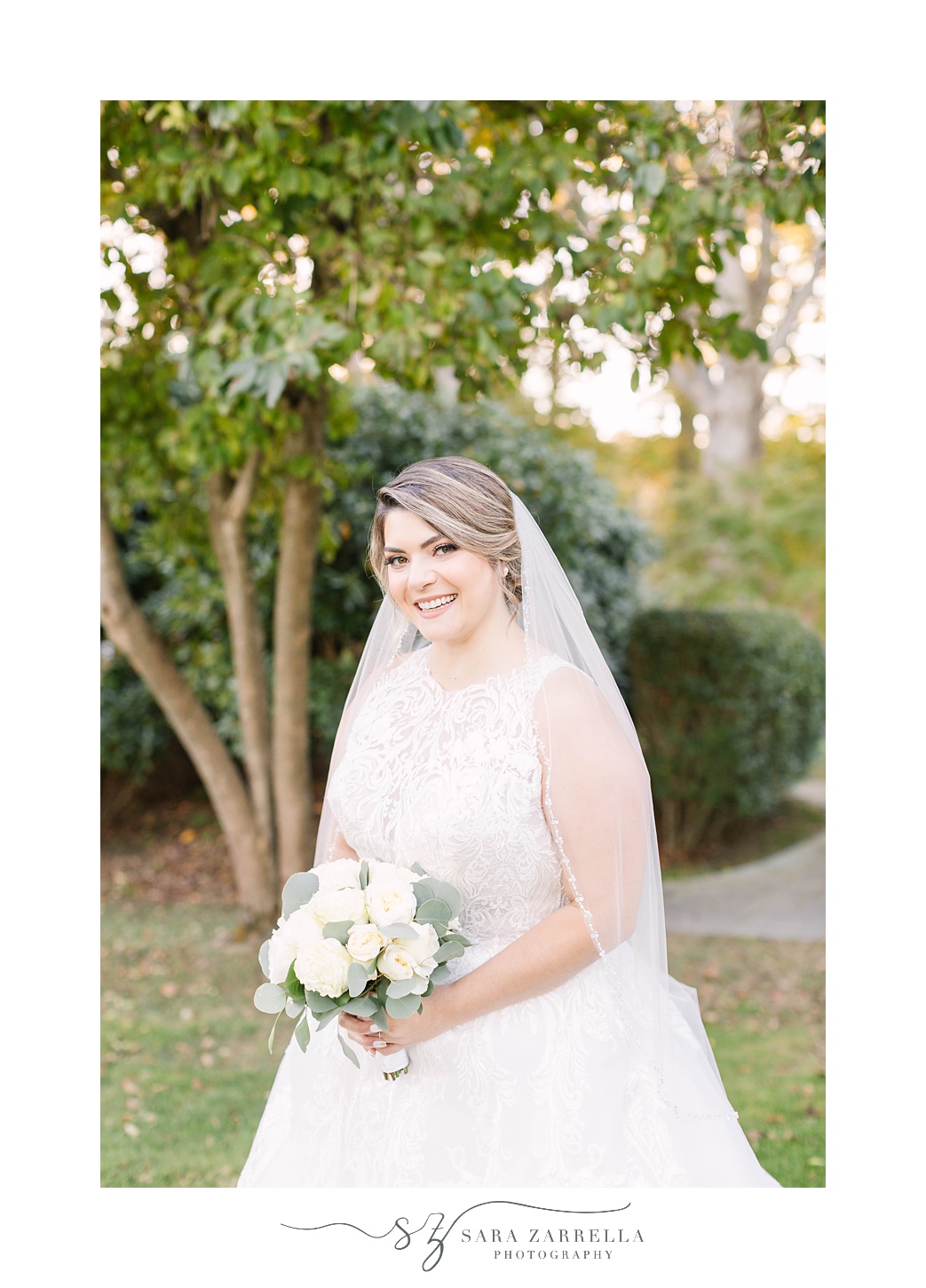 bride holds bouquet of white flowers with veil around shoulders 