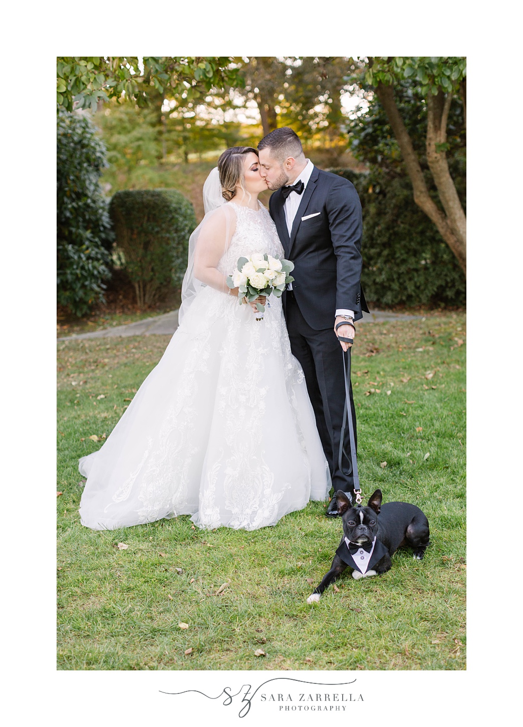 newlyweds kiss while dog lays in grass