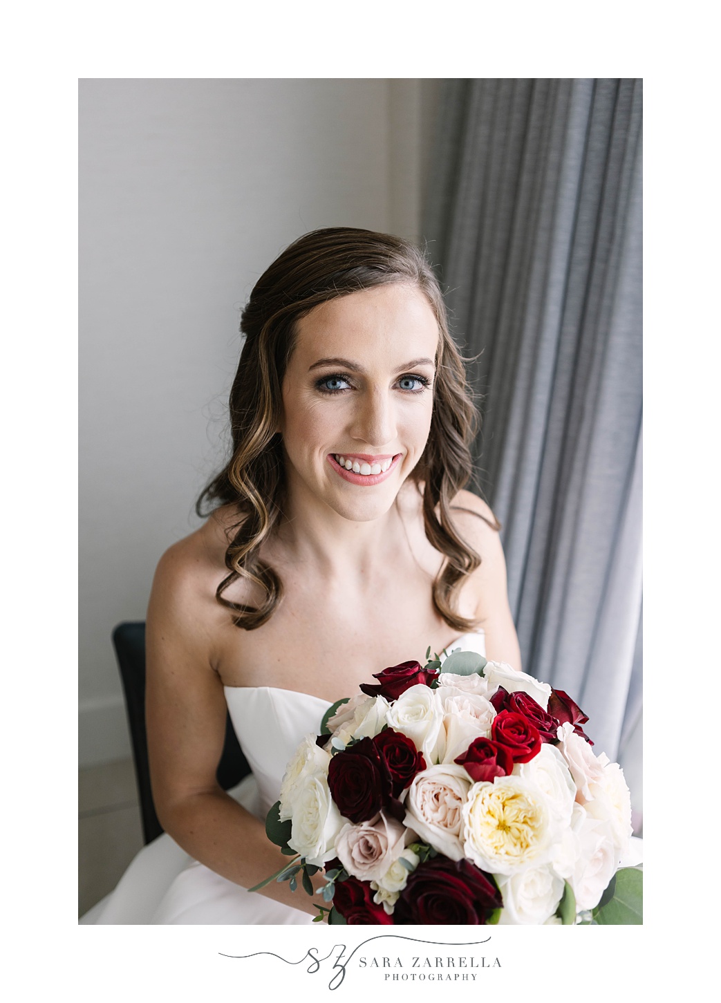 bride sits holding bouquet of red and white flowers for winter wedding
