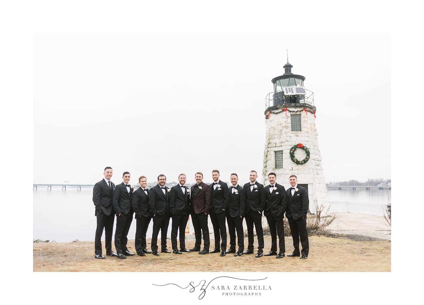 groom and groomsmen pose by lighthouse during winter wedding day