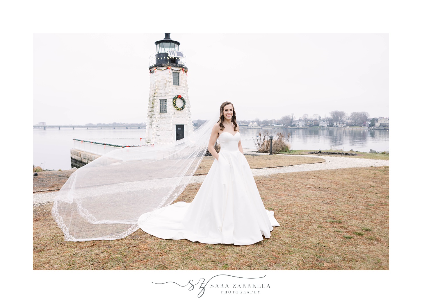 bride stands by lighthouse with veil floating behind her