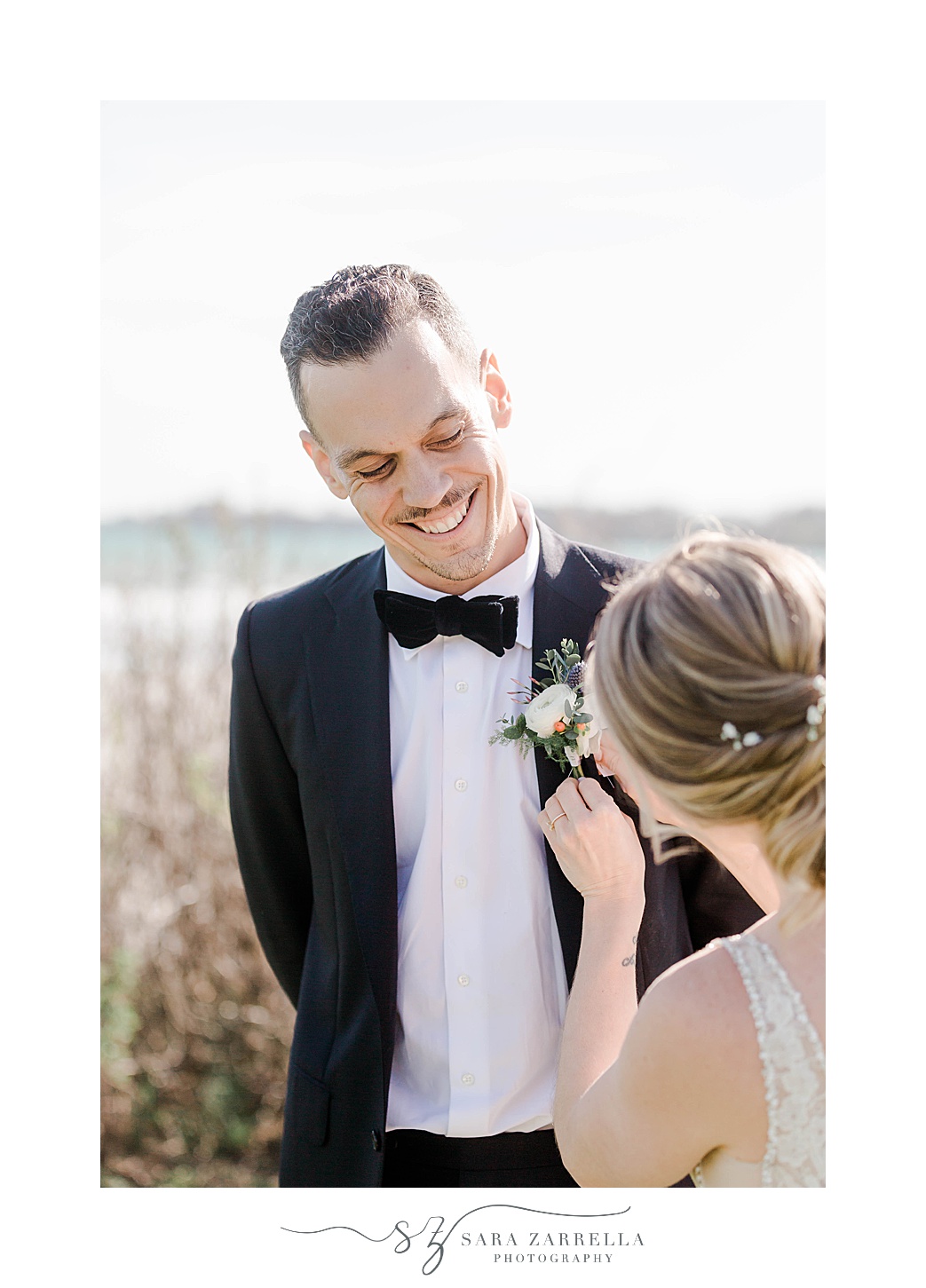 groom smiles at bride while she pins boutonnière 