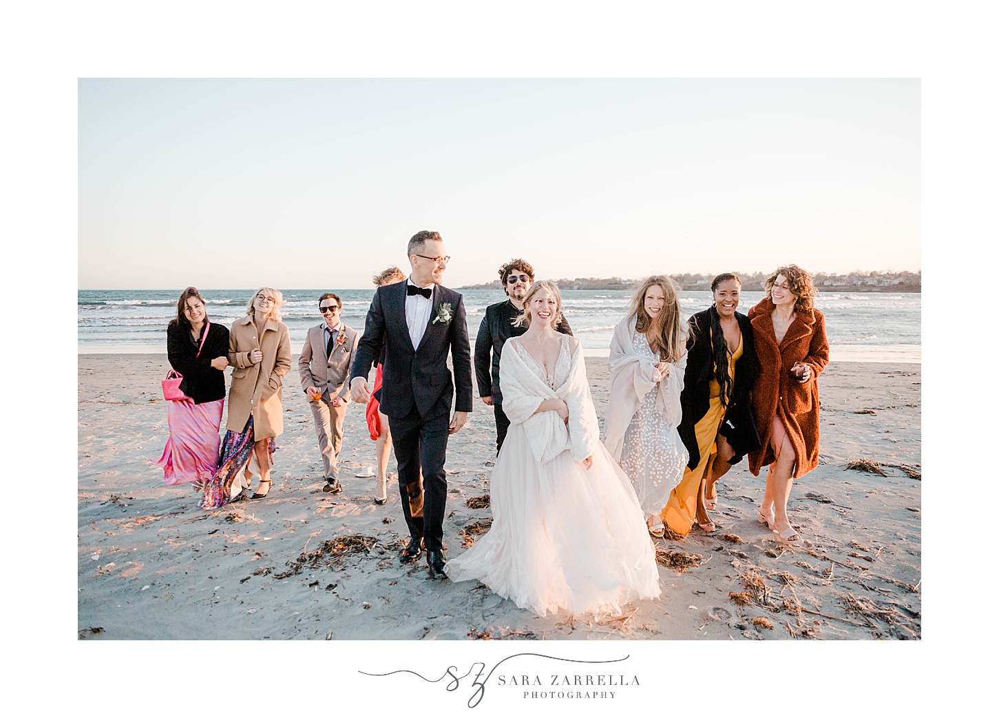 newlyweds walk on beach with wedding party in mismatched gowns