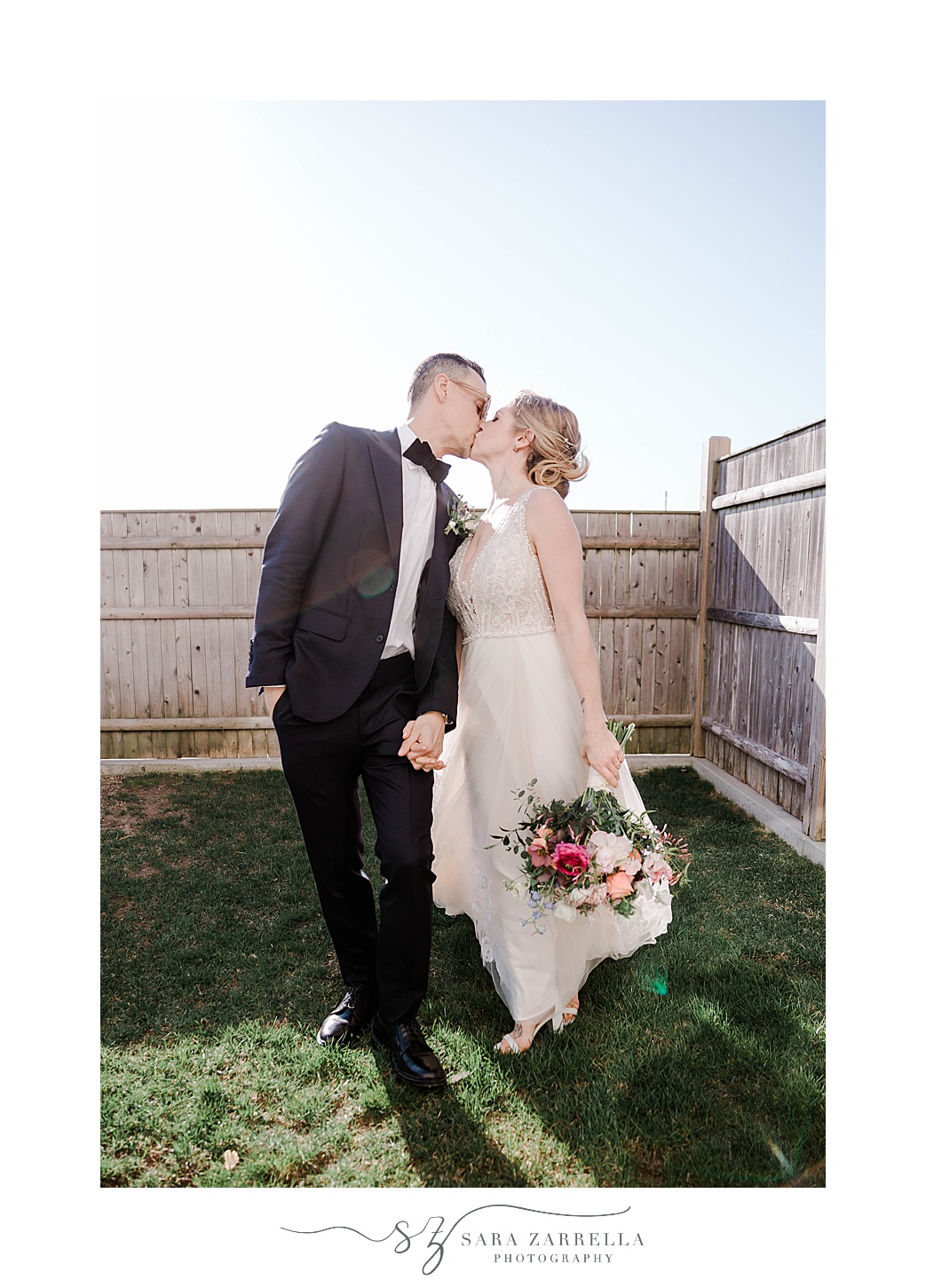 bride and groom kiss in yard with wooden fence at Newport Beach House
