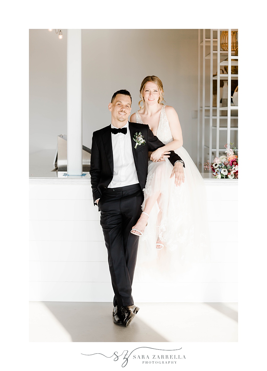 groom leans arm on bride's leg sitting on white wall at Newport Beach House