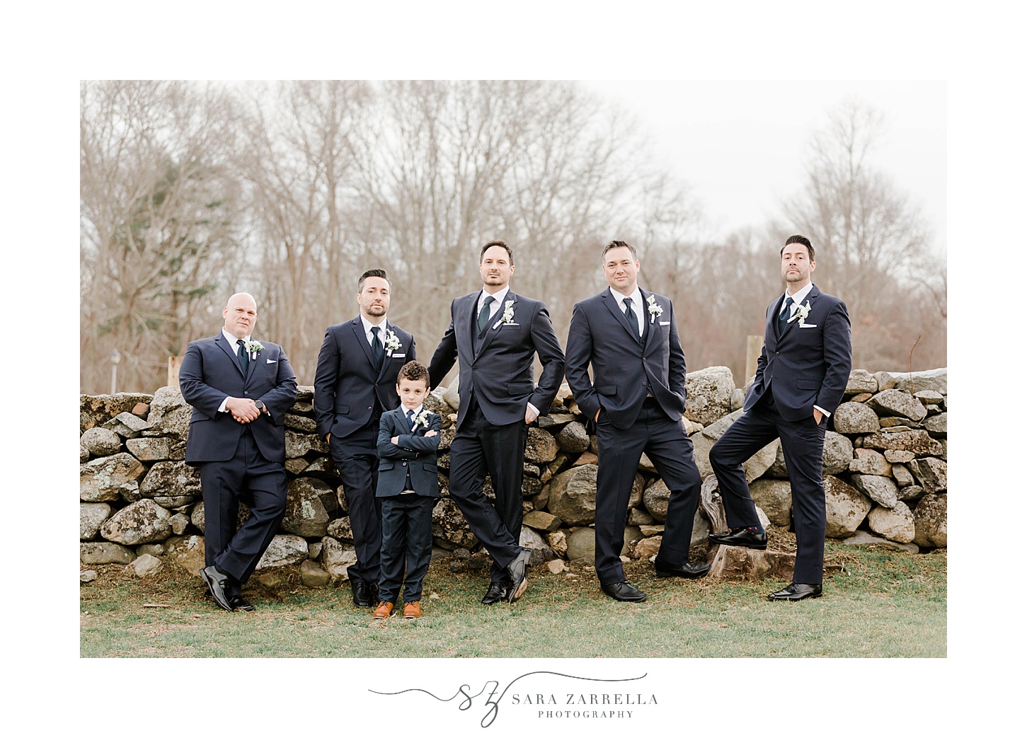 groom and groomsmen in black suits pose by stone wall at Shepard's Run