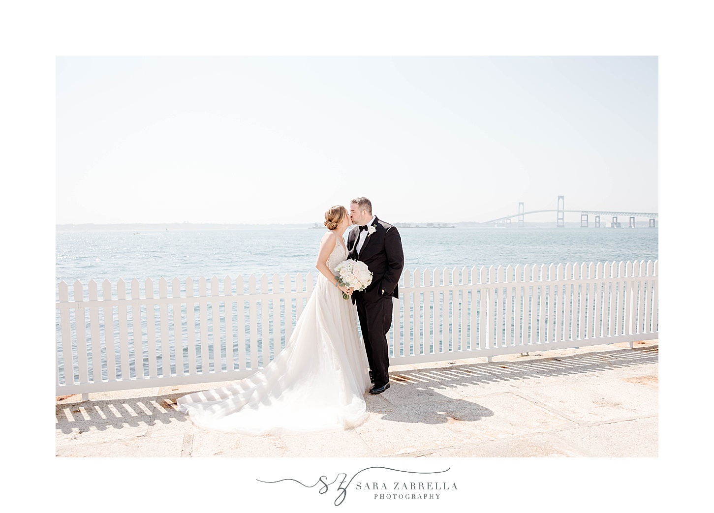 newlyweds kiss against white fence of Gurney's Newport Resort
