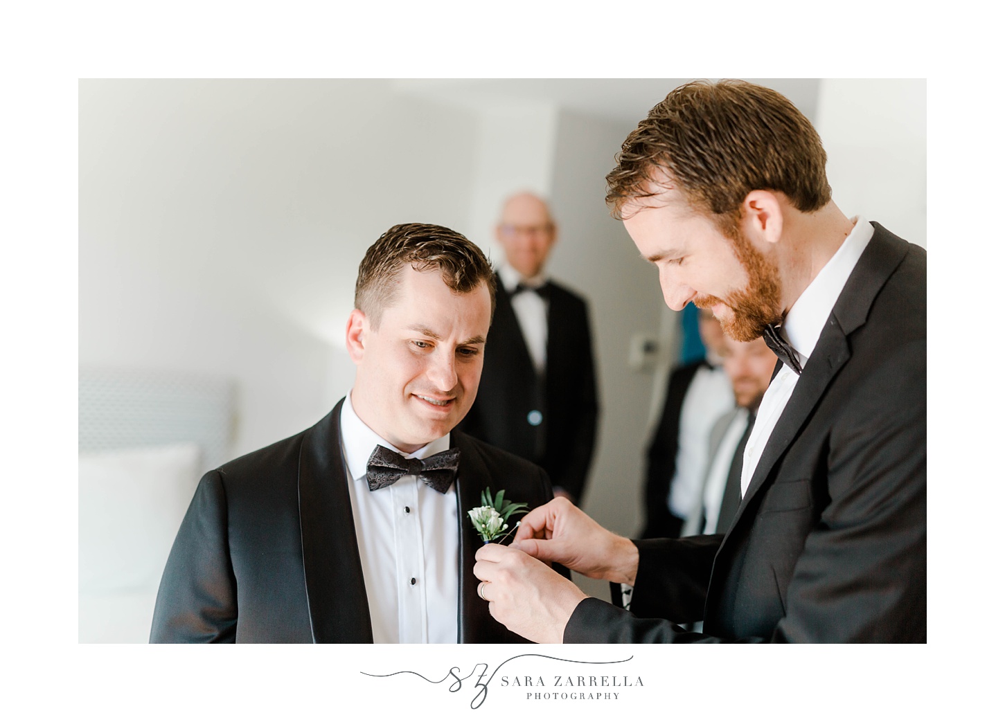 groomsman helps groom with boutonniere 