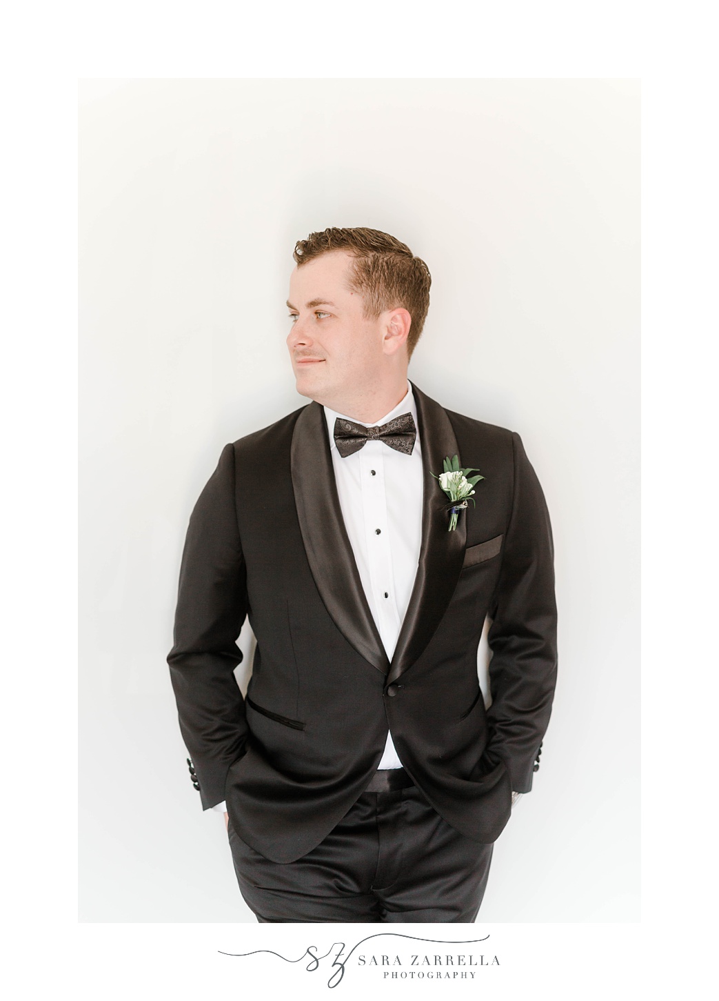 groom in black suit jacket leans against white wall Newport Beach House