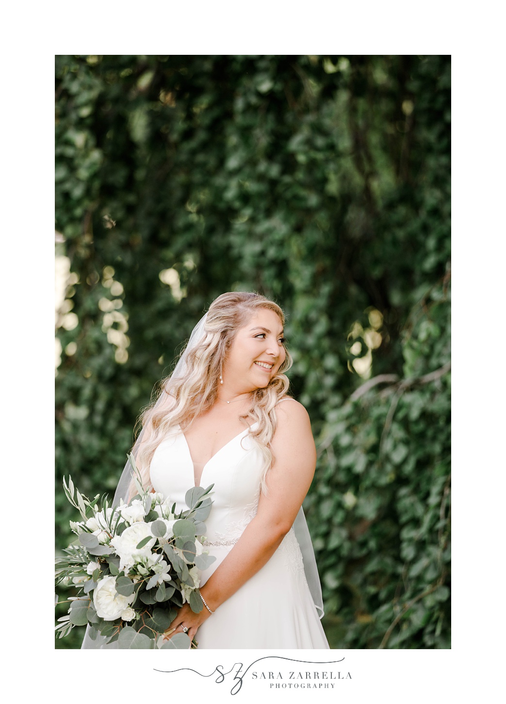 bride holds all-white bouquet looking over shoulder at trees