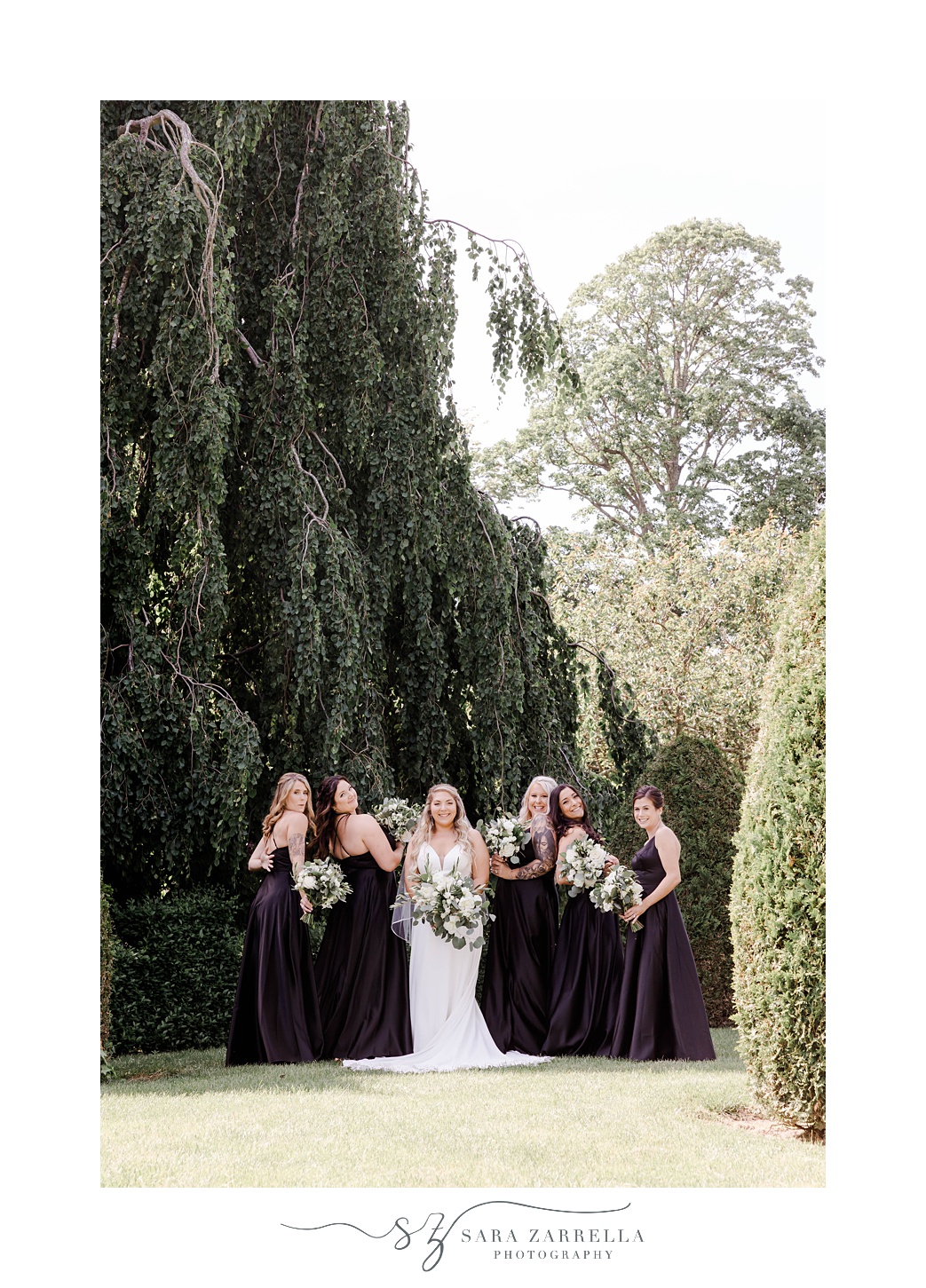 bride stands with bridesmaids by tall hedges at The Elms