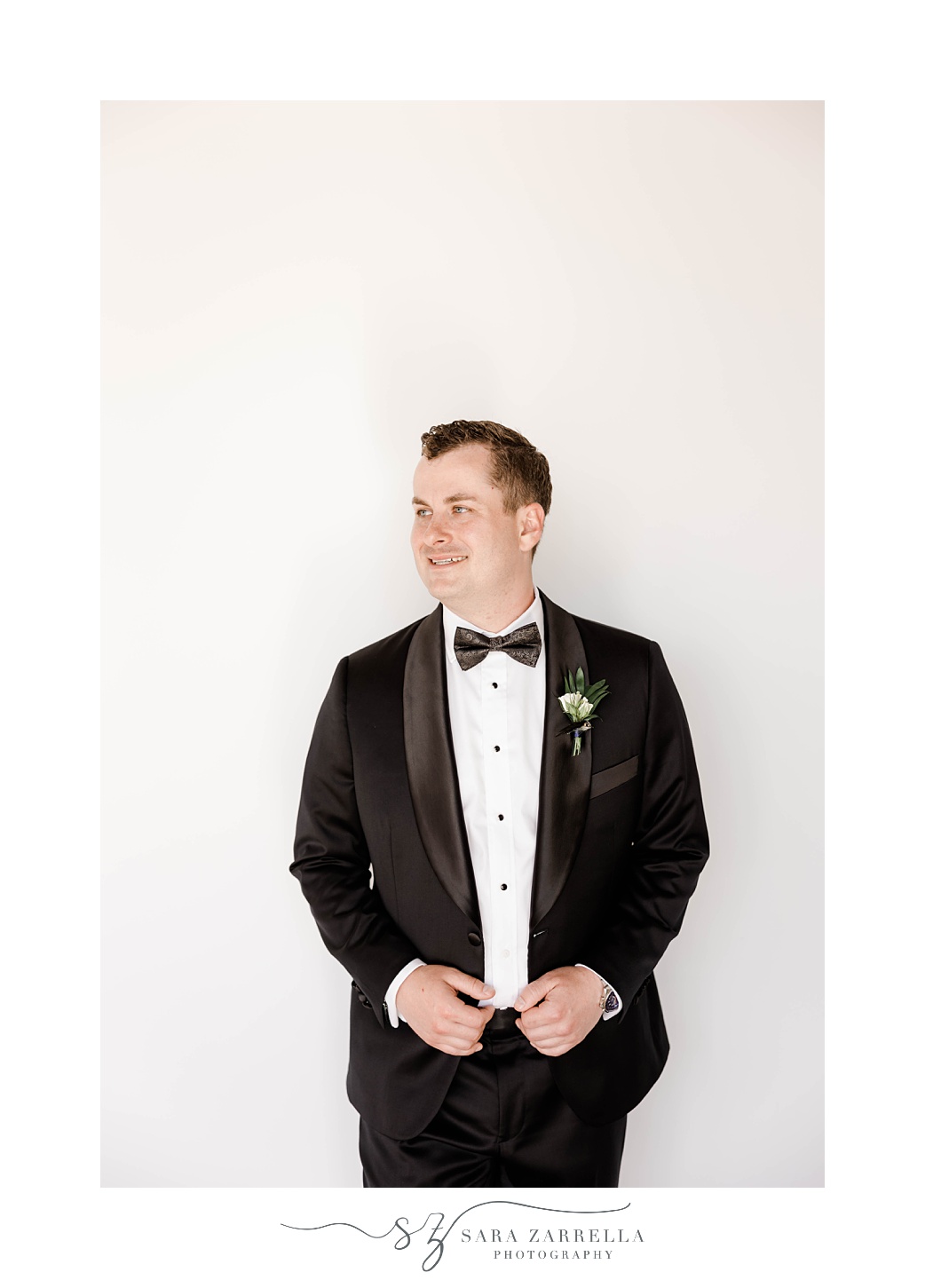 groom leans against wall holding the edge of his suit jacket