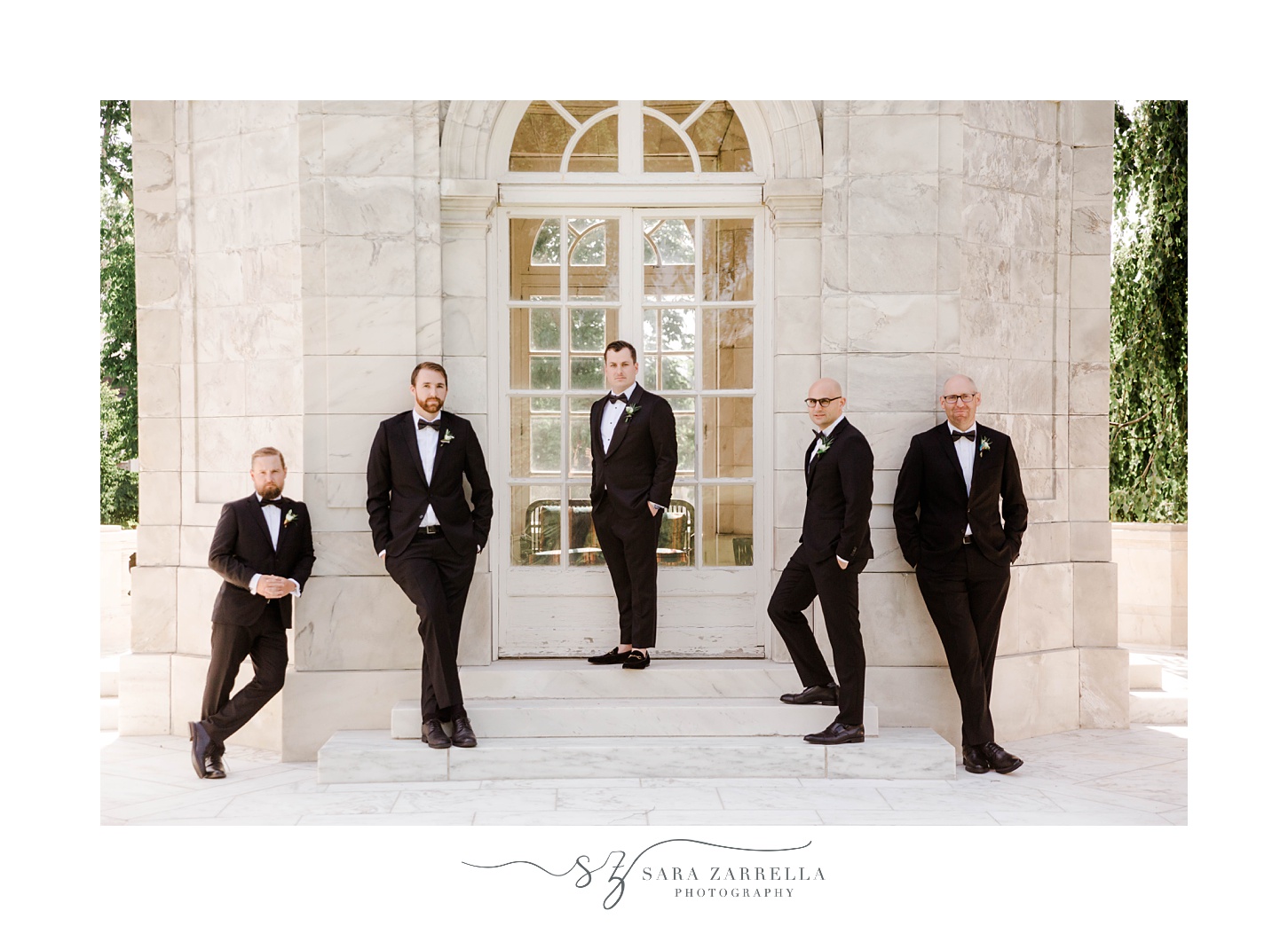 groom stands with groomsmen on marble steps at The Elms 