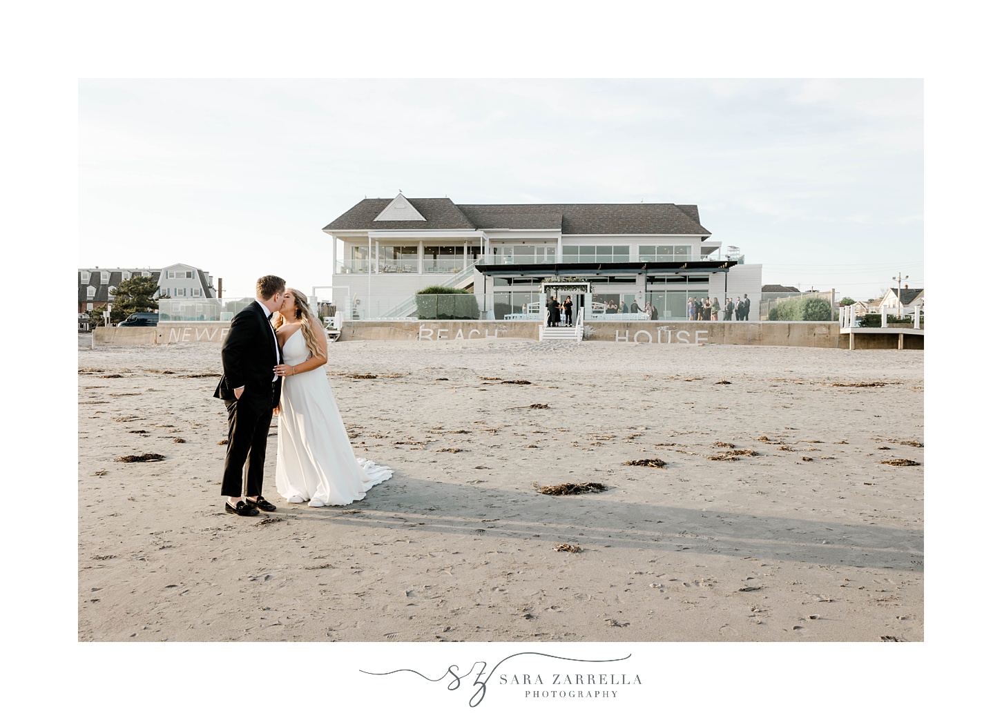 bride and groom kiss on beach in front of Newport Beach House