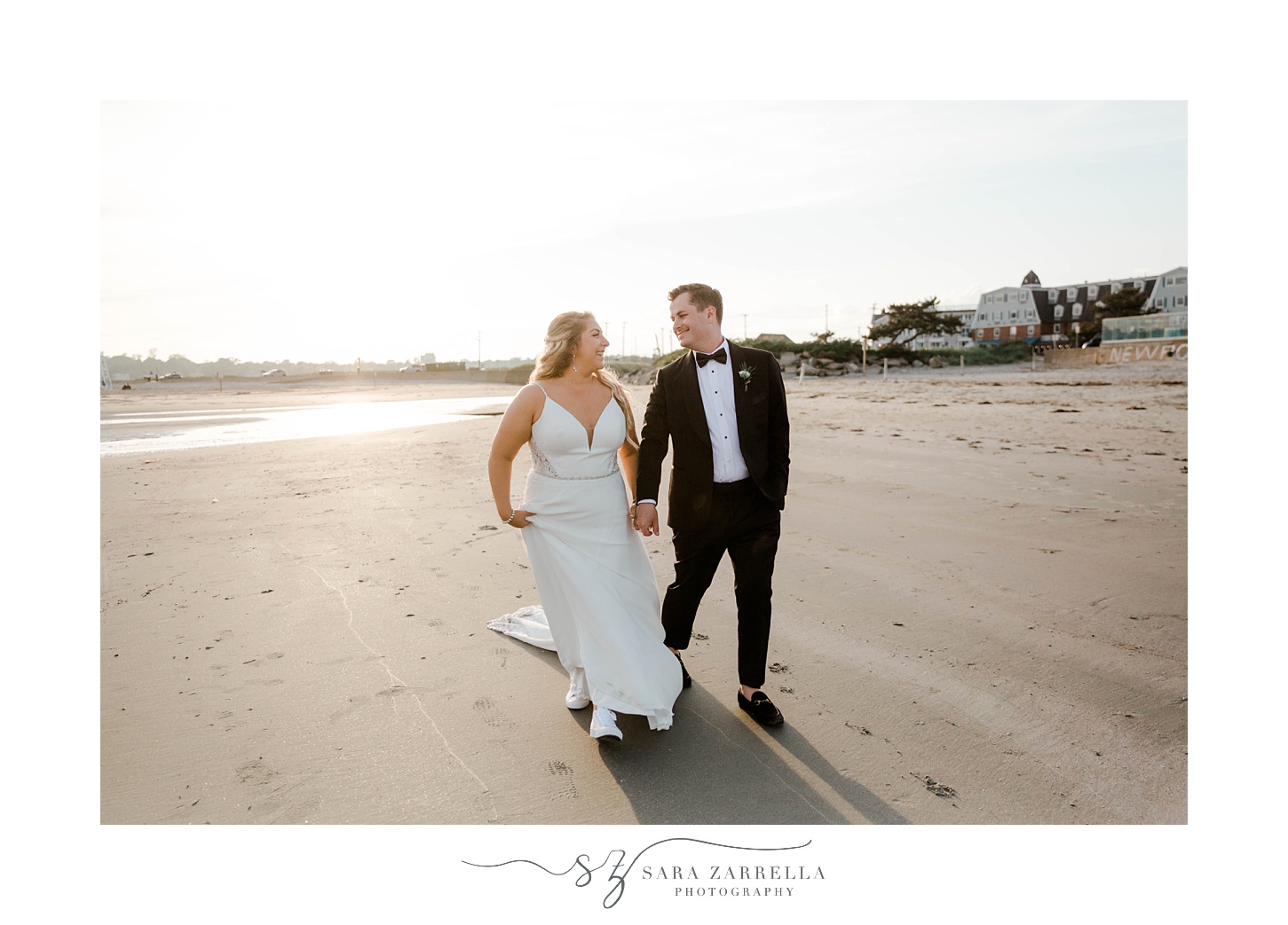 newlyweds hold hands walking along beach at sunset 