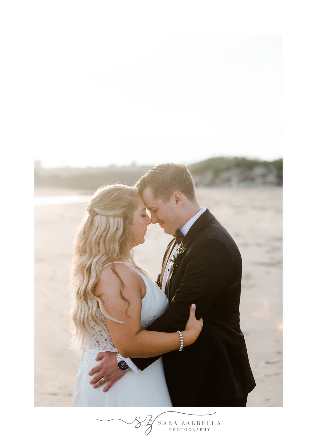 bride and groom lean foreheads together on beach at sunset