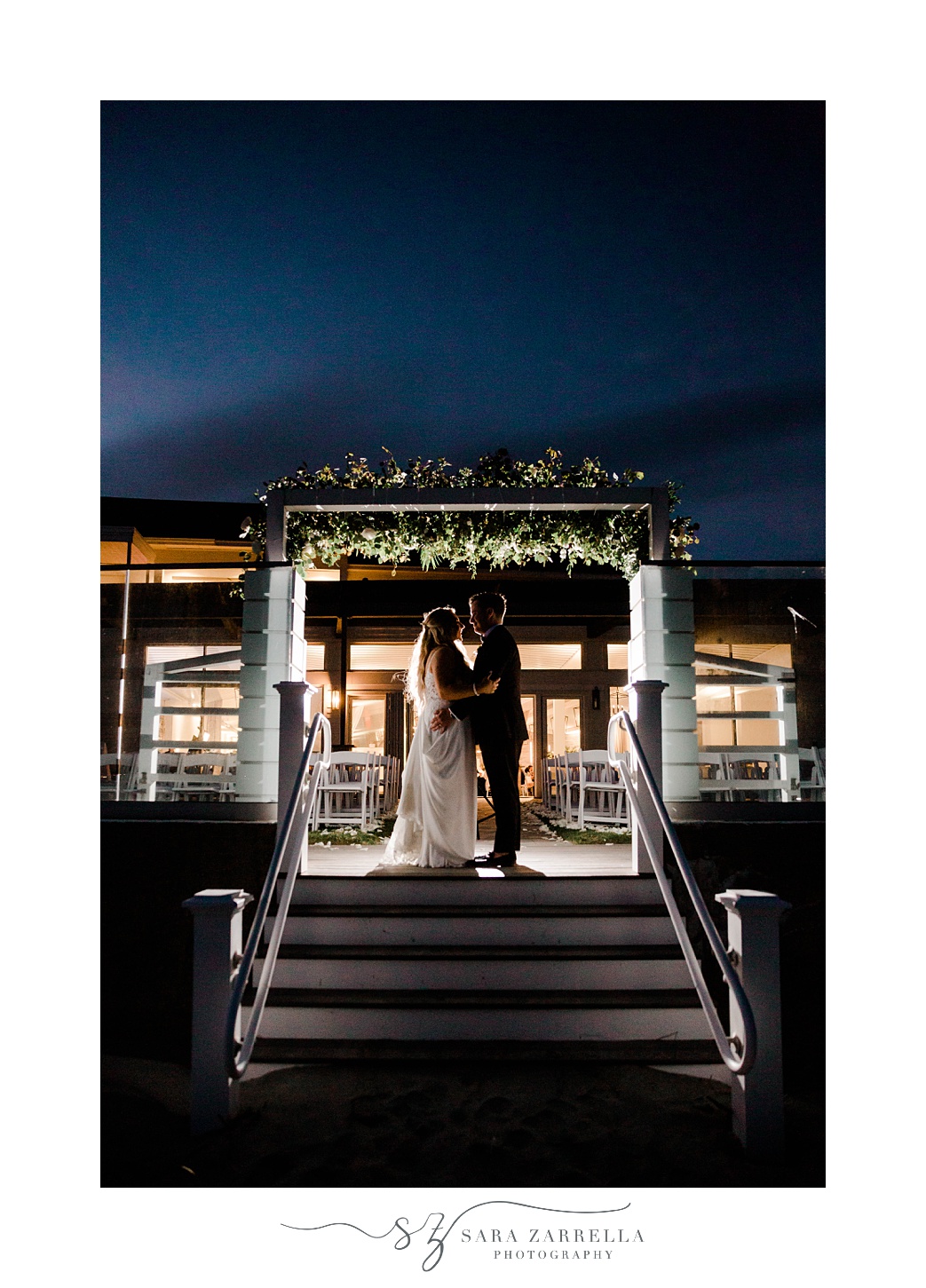 bride and groom pose under arbor at Newport Beach House at night