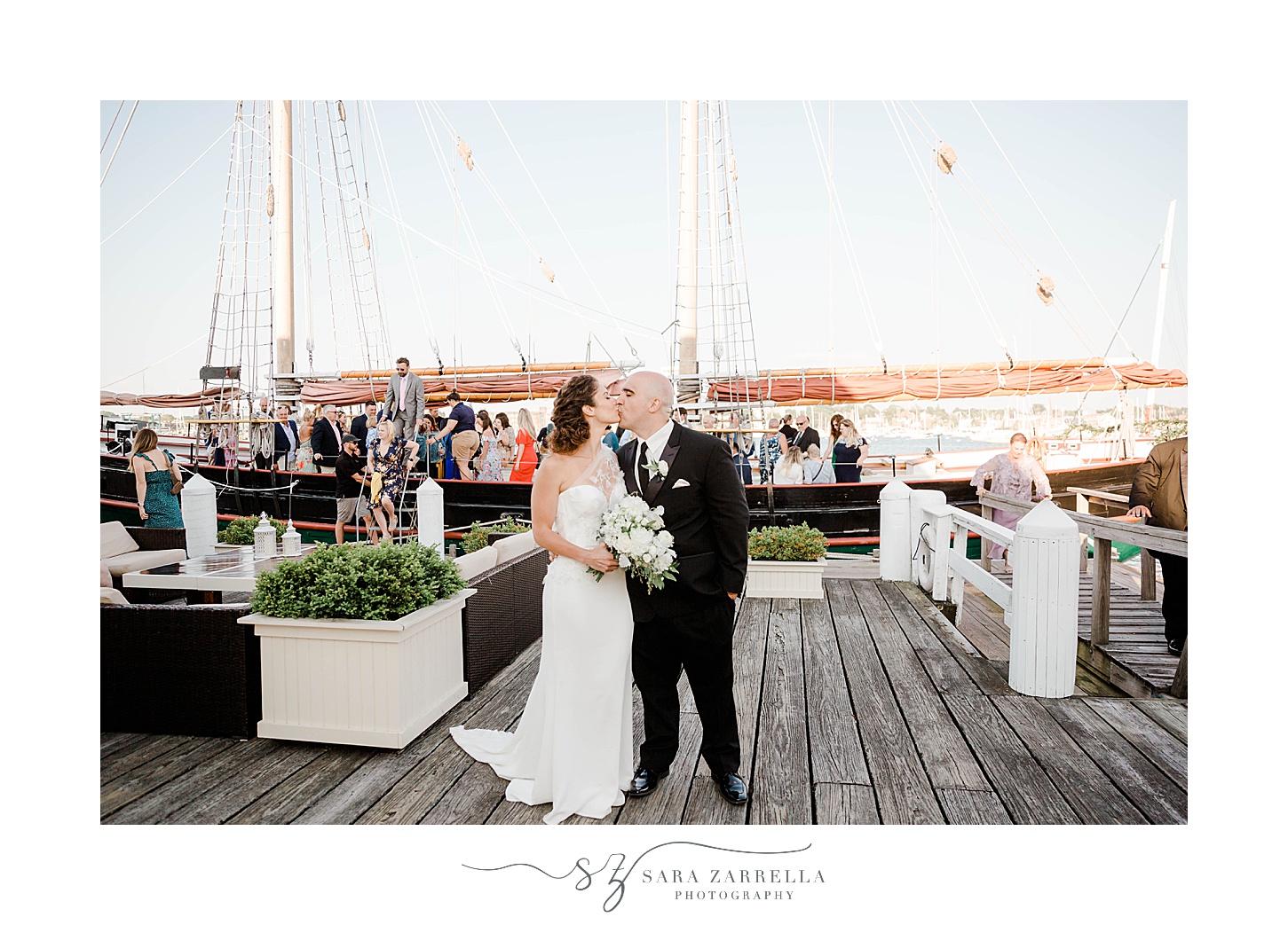 newlyweds kiss on dock with guests standing on the schooner Aurora