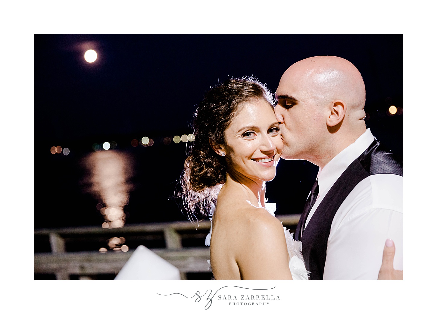 groom kisses bride's cheek during nighttime wedding portraits in Newport RI