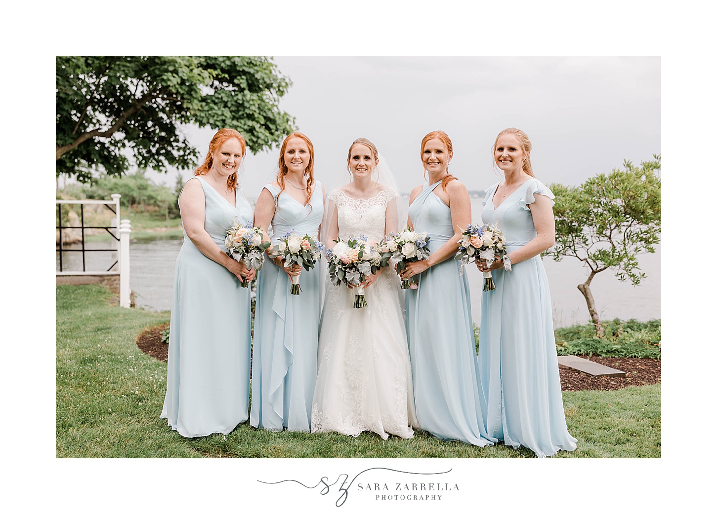 bride stands with bridesmaids in light blue gowns on lawn at Squantum Association