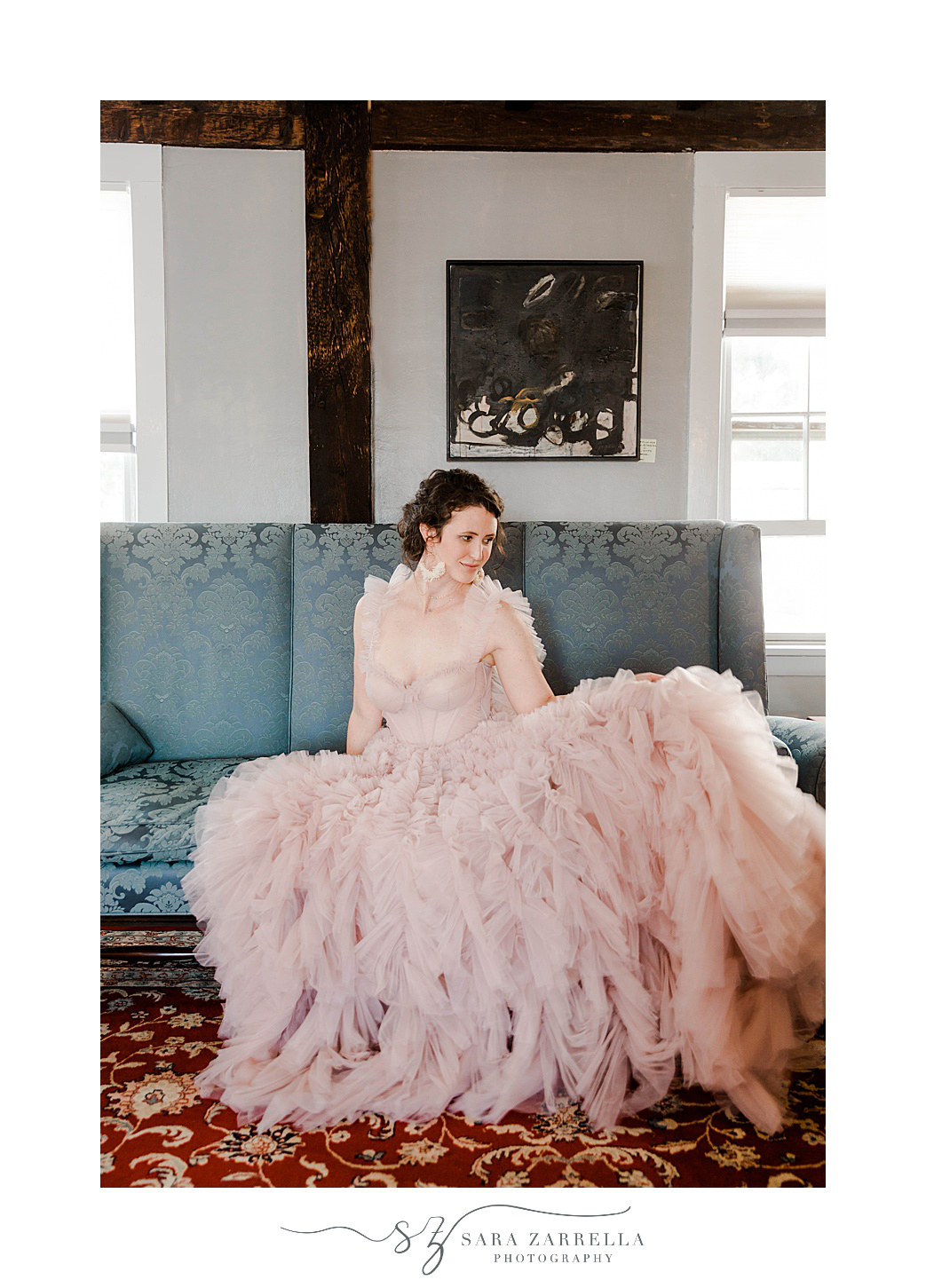 bride sits on blue couch in fluffy pink dress