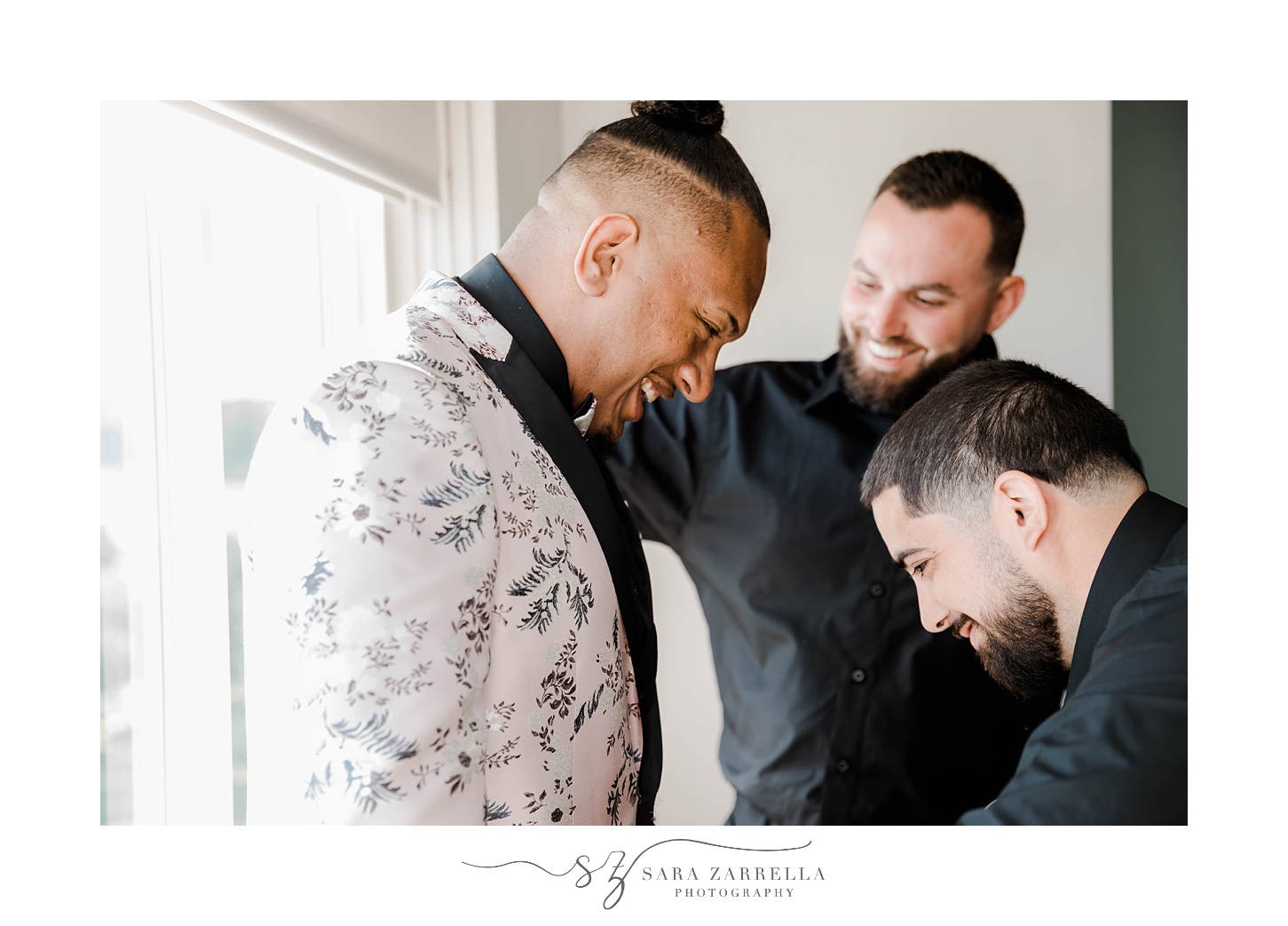 groom laughs with groomsmen looking at his custom suit jacket 