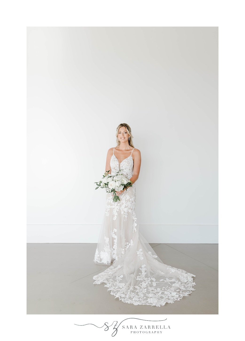bride poses against white wall at Newport Beach House holding bouquet