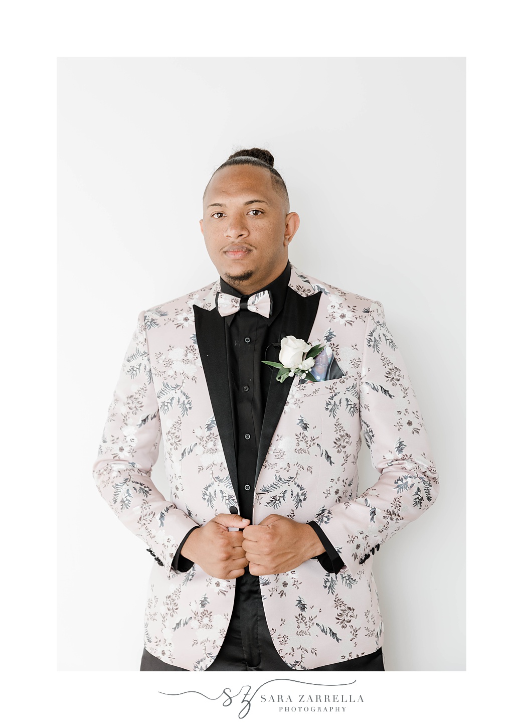 groom adjusts custom suit jacket against white wall 