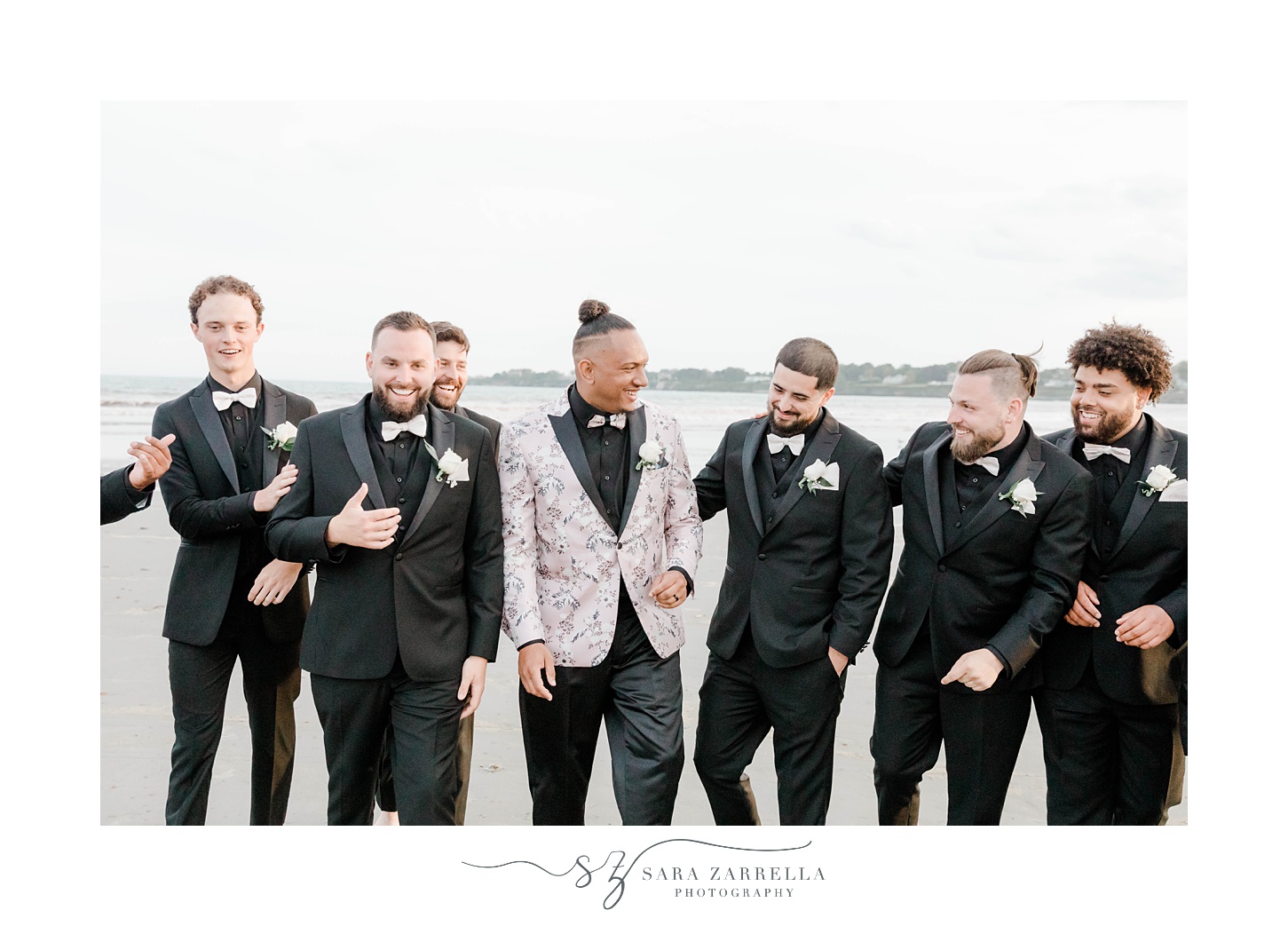 groom laughs with groomsmen walking on beach in Newport RI