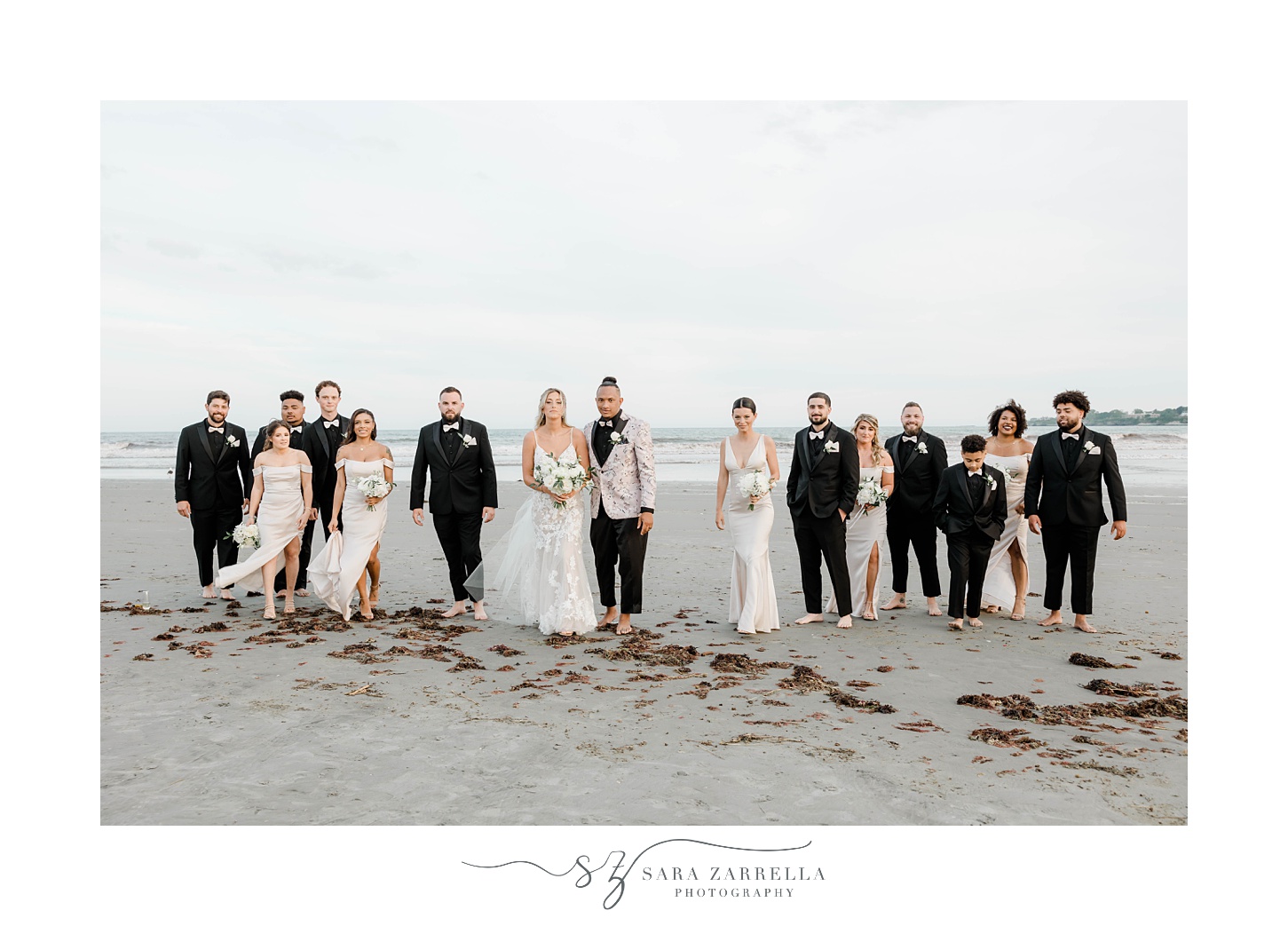 newlyweds stand on beach with wedding party in sand