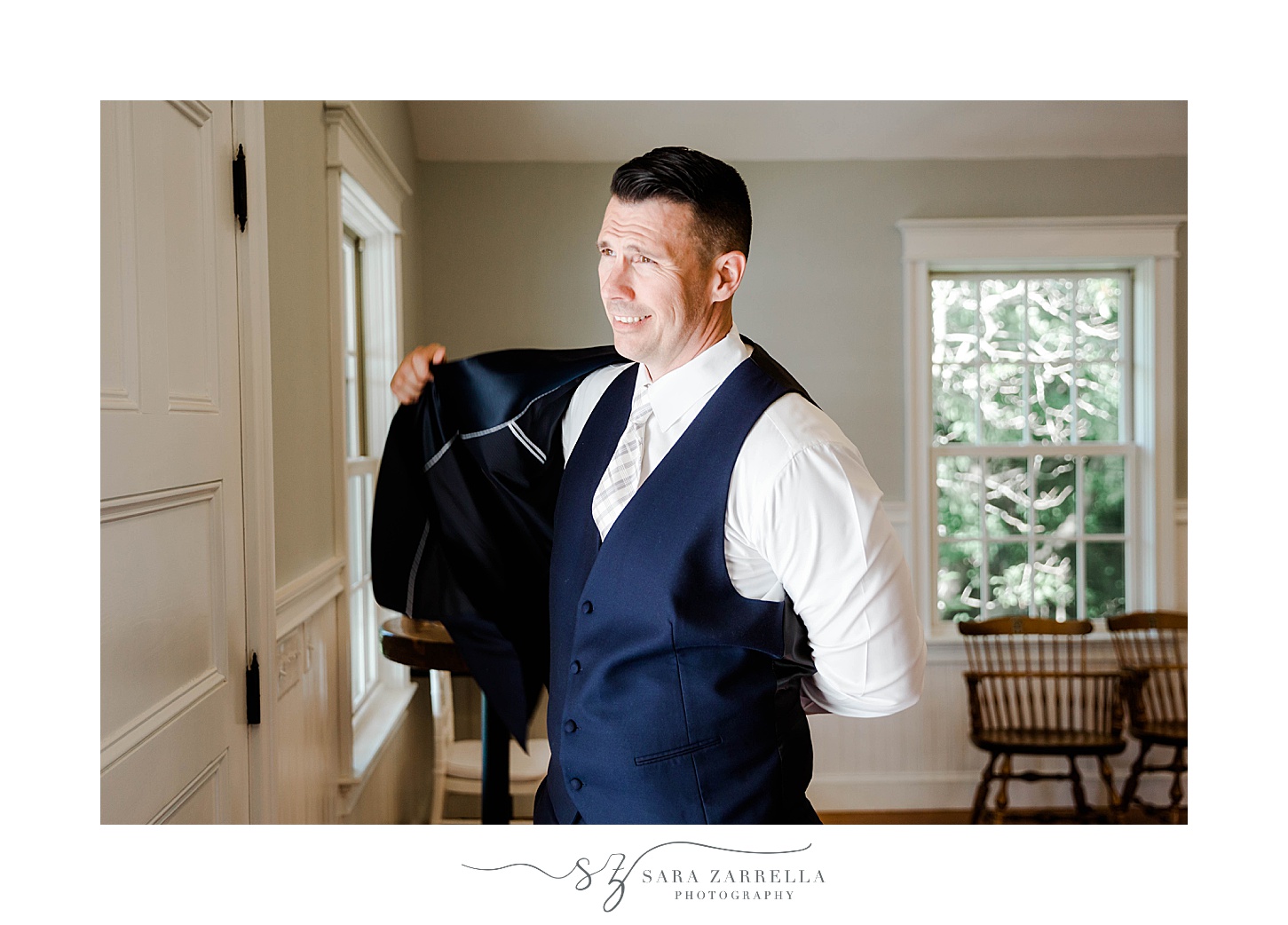 groom puts on navy jacket during prep for RI wedding day