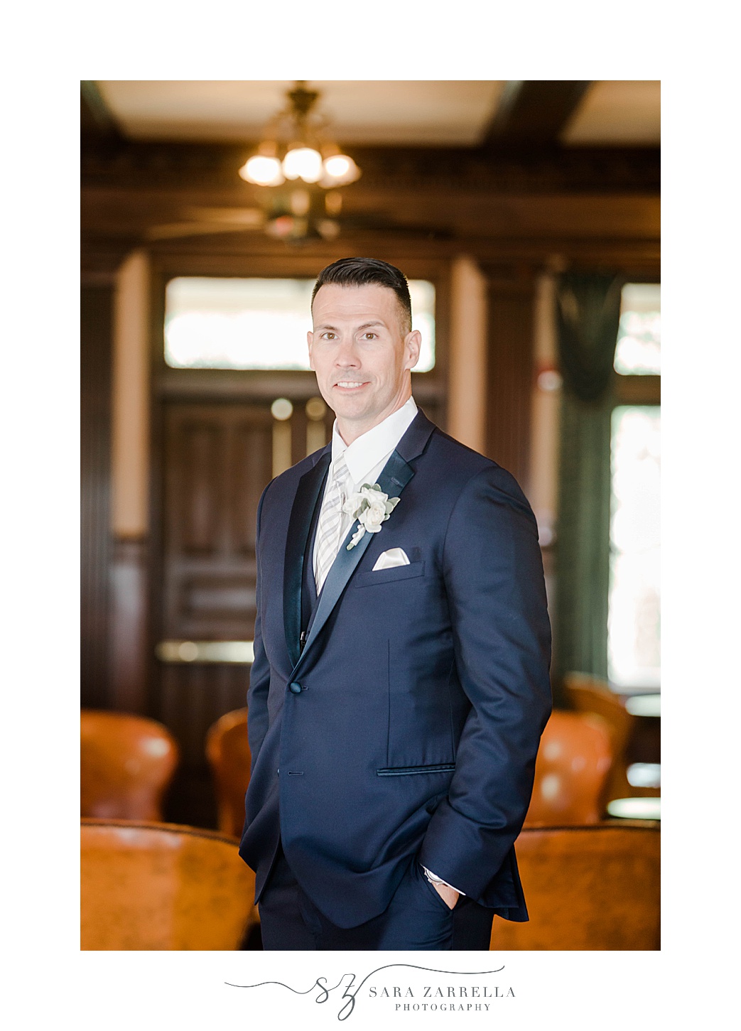 groom stands in navy suit in lobby of Squantum Association