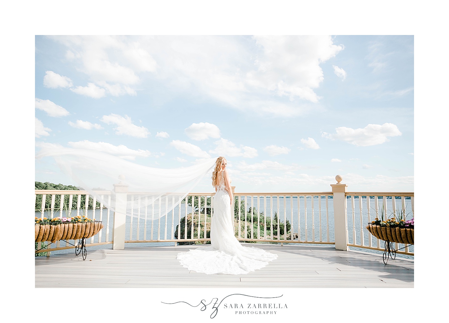 bride poses on balcony overlooking water at Squantum Association with veil floating