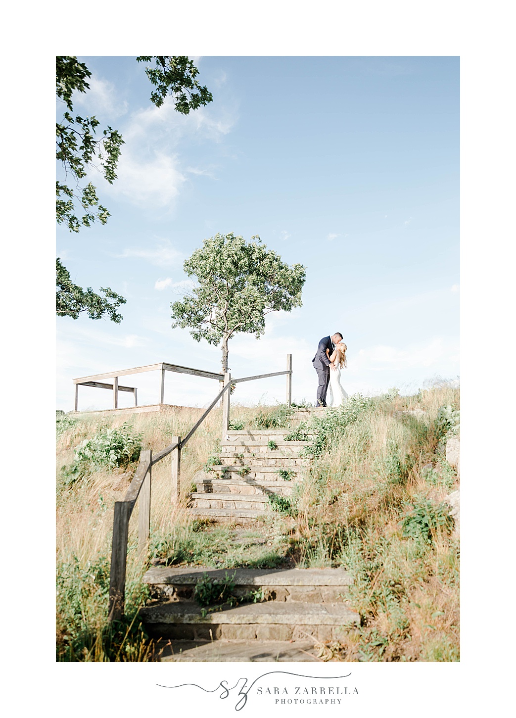 bride and groom kiss at top of hill against blue sky