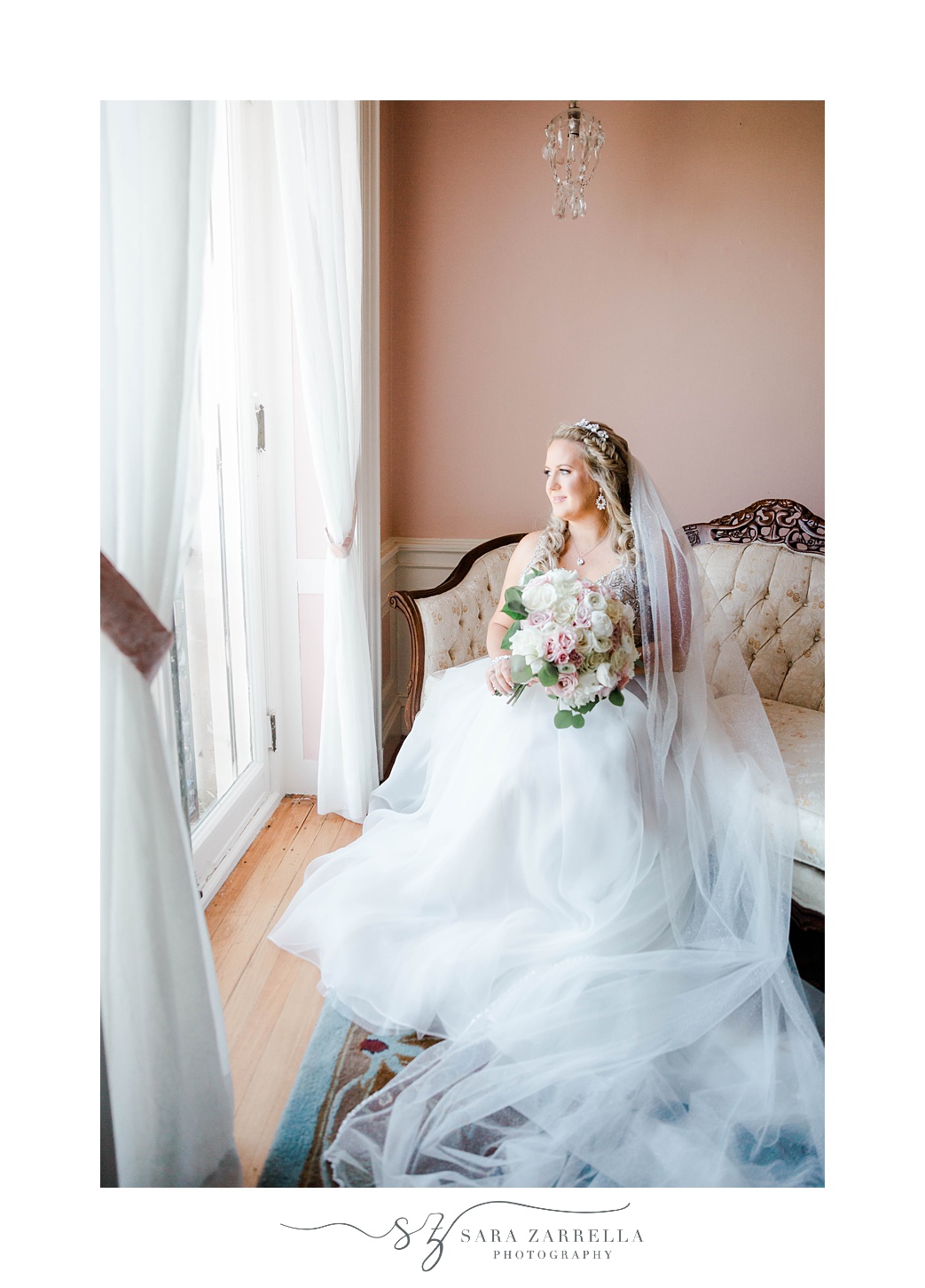 bride sits on ivory couch with veil draped around her before Aldrich Mansion wedding